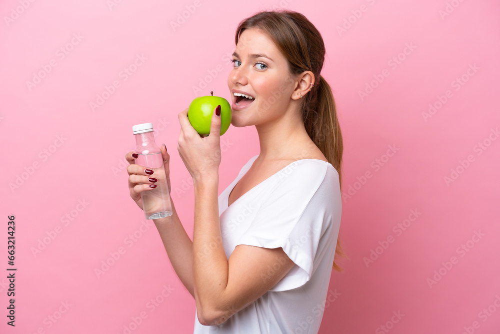 Young caucasian woman isolated on pink background with an apple and with a bottle of water Young caucasian woman isolated on pink background with an apple and with a bottle of water