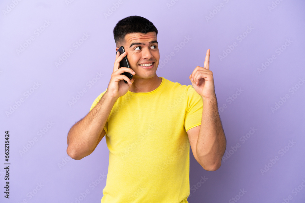 Young handsome man using mobile phone over isolated purple background pointing up a great idea Young handsome man using mobile phone over isolated purple background pointing up a great idea