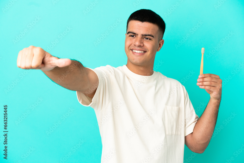 Fototapeta premium Young handsome man brushing teeth over isolated blue background giving a thumbs up gesture