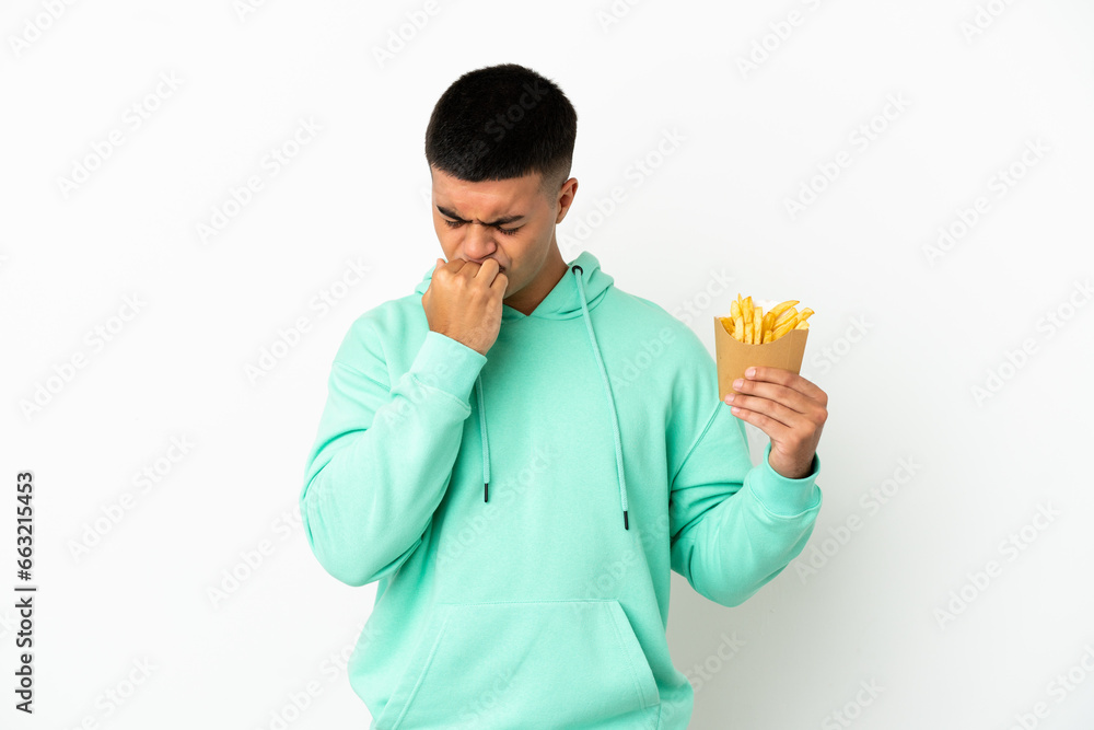 Young handsome man holding fried chips over isolated white background having doubts Young handsome man holding fried chips over isolated white background having doubts