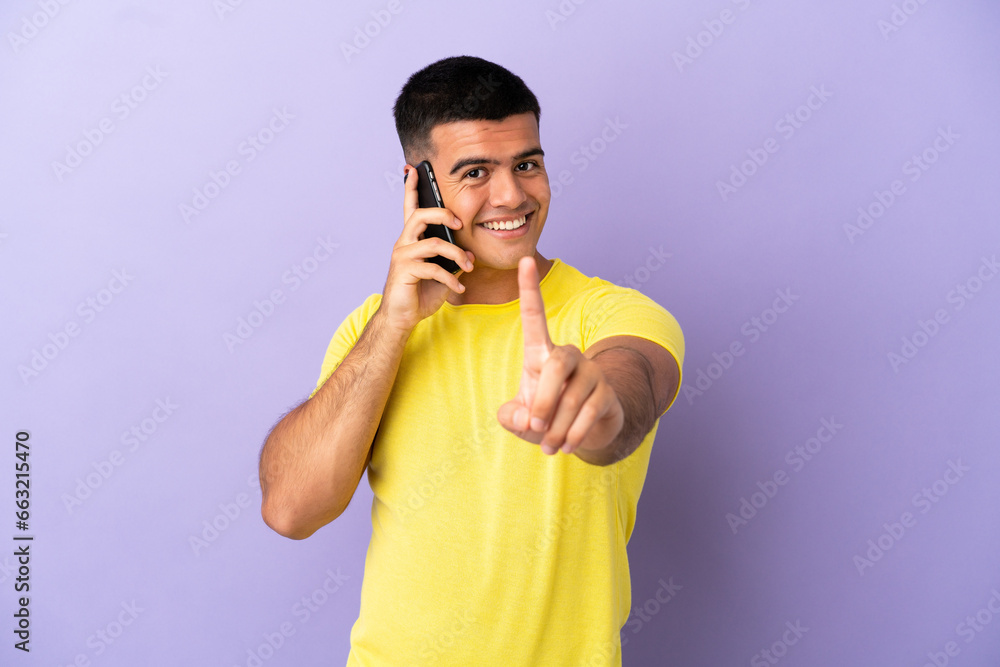 Young handsome man using mobile phone over isolated purple background showing and lifting a finger Young handsome man using mobile phone over isolated purple background showing and lifting a finger