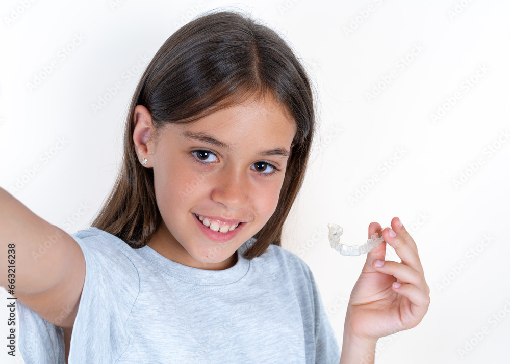 Beautiful little kid girl wearing blue T-shirt make selfie holding an invisible braces aligner, recommending this new treatment. Dental healthcare concept. Beautiful little kid girl wearing blue T-shirt make selfie holding an invisible braces aligner, recommending this new treatment. Dental healthcare concept.