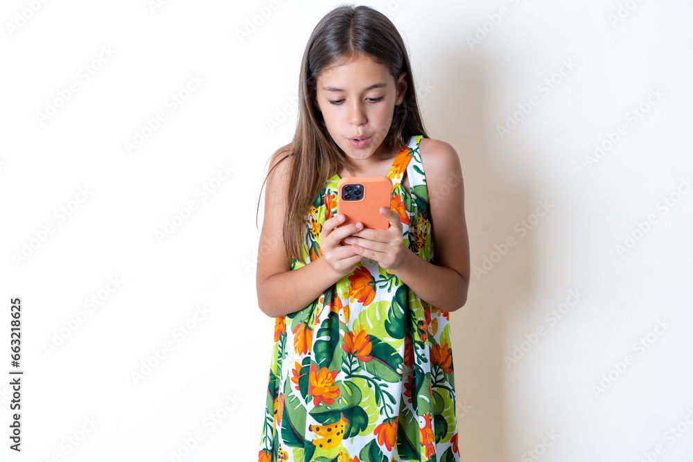 Portrait of an excited Beautiful kid girl wearing floral dress playing games on mobile phone. Portrait of an excited Beautiful kid girl wearing floral dress playing games on mobile phone.