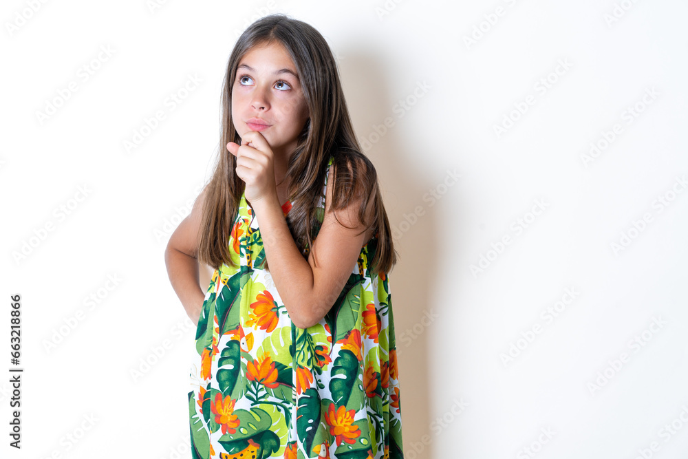Thoughtful Beautiful kid girl wearing floral dress holds chin and looks away pensively makes up great plan Thoughtful Beautiful kid girl wearing floral dress holds chin and looks away pensively makes up great plan