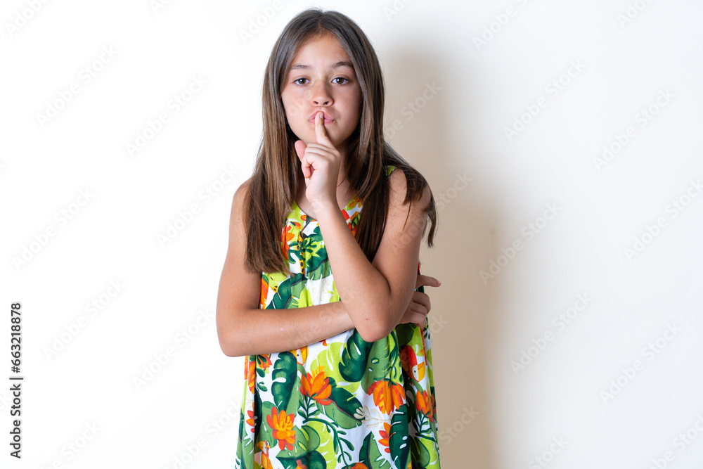 Beautiful kid girl wearing floral dress silence gesture keeps index finger to lips makes hush sign. Asks not to share secret Beautiful kid girl wearing floral dress silence gesture keeps index finger to lips makes hush sign. Asks not to share secret