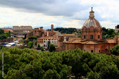 Photo of a panoramic view of the historic part of the city with a church and the Colosseum in the background and green areas in the foreground in the city of Rome, Lazio region, Italy