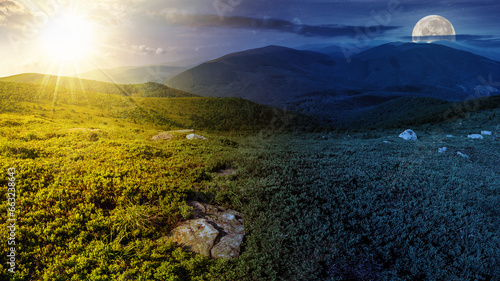Obraz na płótnie mountain panorama landscape with sun and moon at twilight. stones in grass on top of the hillside of mountain range. day and night time change concept. mysterious countryside scenery in morning light w salonie
