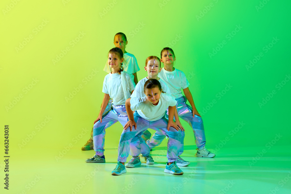 Team of smiling attractive girls children dressed in fashion, stylish outfit dancing in choreography class isolated on green-yellow gradient background. - obrazy, fototapety, plakaty 
