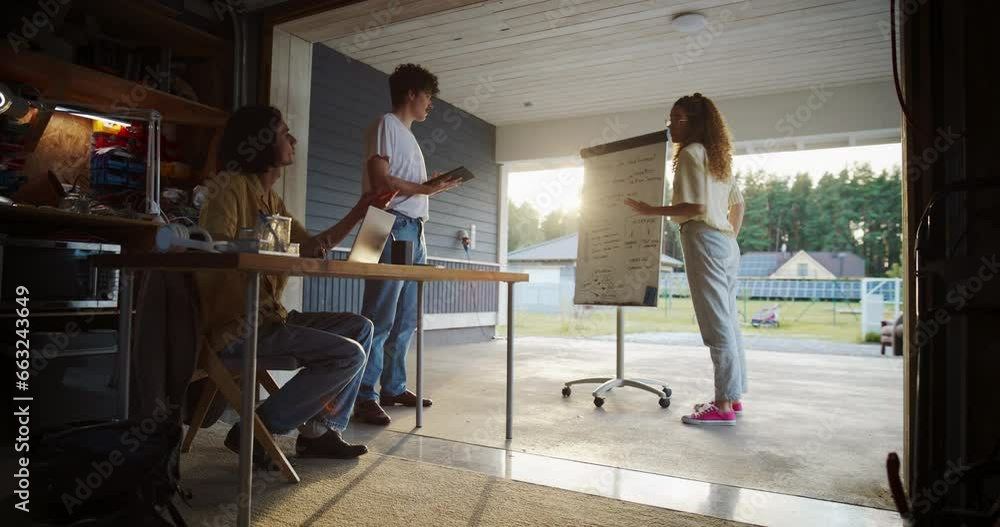 Diverse Team Of Young Entrepreneurs Having A Meeting In Home Garage. Hispanic Female CEO Using Whiteboard To Explain Business Objectives To Two Caucasian Male Colleagues With Laptop And Tablet. Diverse Team Of Young Entrepreneurs Having A Meeting In Home Garage. Hispanic Female CEO Using Whiteboard To Explain Business Objectives To Two Caucasian Male Colleagues With Laptop And Tablet.
