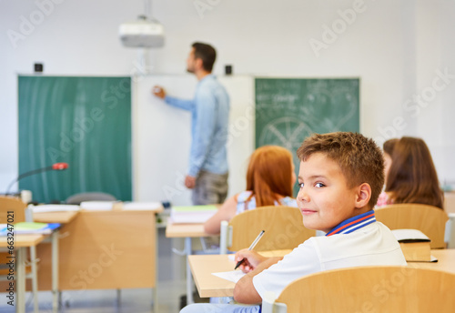 Smiling schoolboy sitting on bench in classroom