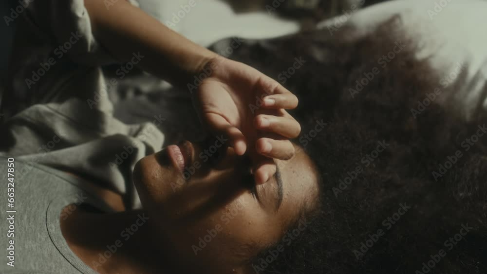 African American teenage girl lying down on bed and holding hand on face while suffering from depression African American teenage girl lying down on bed and holding hand on face while suffering from depression