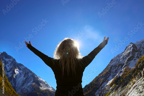 hands spread to sides. female Hiker arms outstretched on mountain top. woman on snowy mountain covered pine forest. woman on peak of Caucasian Mountain. back, rear view of adult blonde lady. winter