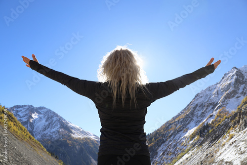 hands spread to sides. female Hiker arms outstretched on mountain top. woman on snowy mountain covered pine forest. woman on peak of Caucasian Mountain. back, rear view of  adult blonde lady. winter