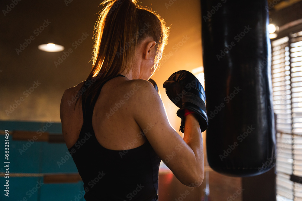 Women self defense girl power. Strong woman fighter training punches on boxing ring. Healthy strong girl punching boxing bag. Training day in boxing gym. Strength fit body workout training