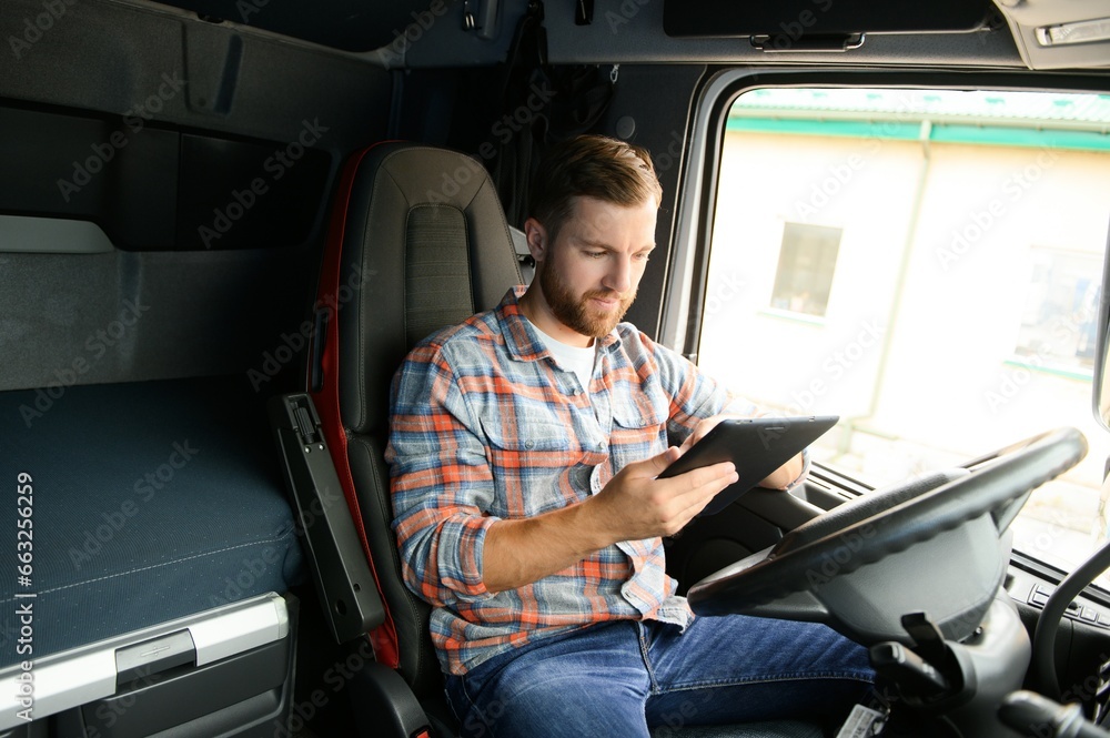 Man truck driver sitting behind wheel of car and holding digital tablet in his hands - obrazy, fototapety, plakaty 
