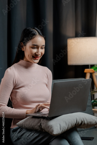 Asian woman in the living room with laptop, female company employee on vacation, using vacation time and free time to relax at home, weekend vacation doing activities. #663256254