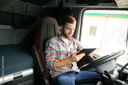 Man truck driver sitting behind wheel of car and holding digital tablet in his hands