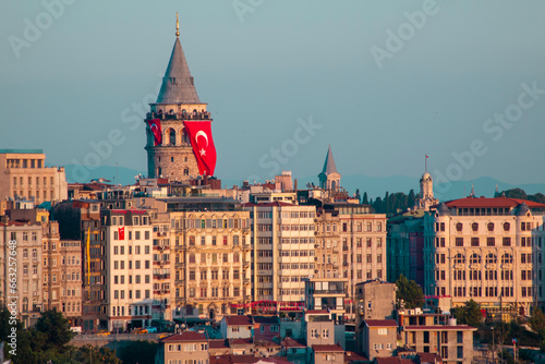 Galata Tower is located in the Beyoğlu district of Istanbul. As the sun sets, its lights reflect on the Galata tower and buildings. The Turkish flag hanging on the Galata Tower. Istanbul, Turkey. © thehakanarslan