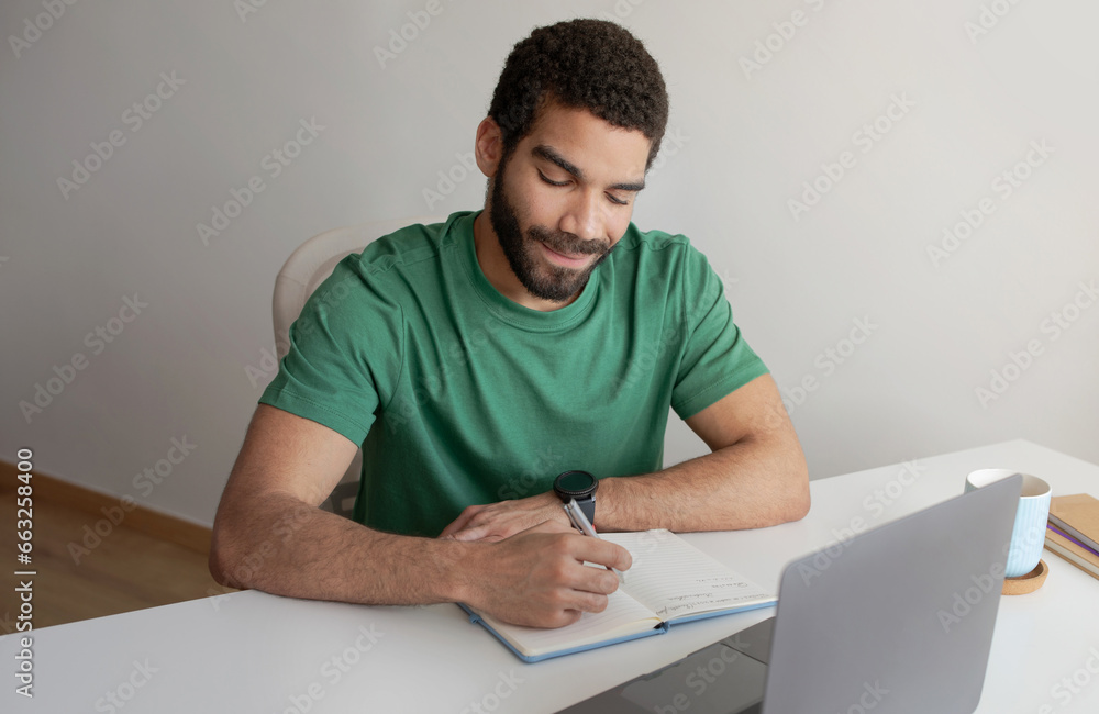 Positive young muslim guy student, manager making notes, works with laptop, create idea for startup Positive young muslim guy student, manager making notes, works with laptop, create idea for startup