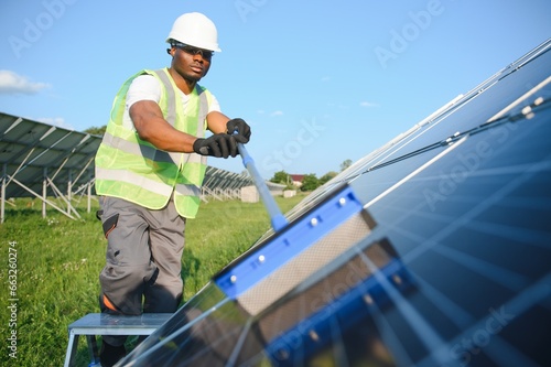 Tidy african american worker is cleaning solar panels with special broom.