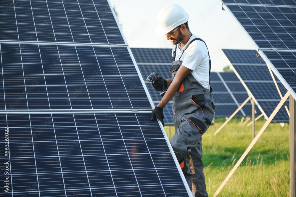 Male arabian engineer in helmet and brown overalls checking resistance in solar panels outdoors. Indian man working on station. Male arabian engineer in helmet and brown overalls checking resistance in solar panels outdoors. Indian man working on station.