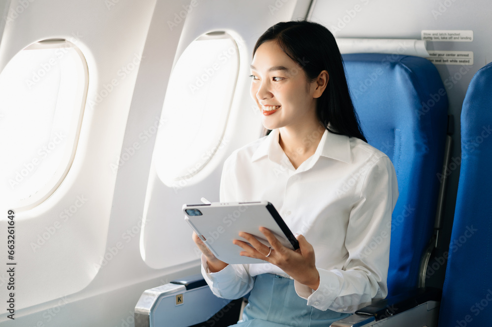 Attractive Asian female passenger of airplane sitting in comfortable seat while working laptop and tablet with mock up area using wireless connection. Travel in style, work with grace.. Attractive Asian female passenger of airplane sitting in comfortable seat while working laptop and tablet with mock up area using wireless connection. Travel in style, work with grace..