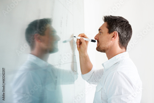 Man, writing on glass board and brainstorming, business ideas at creative startup with agenda and planning. Productivity, schedule or timeline for SEO project, marketing strategy and moodboard