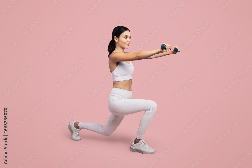 Woman lunging with dumbbells, white attire, pink background