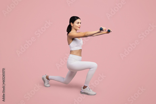 Woman lunging with dumbbells, white attire, pink background