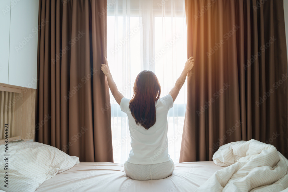 happy woman stretching on bed after wake up, young adult female rising arms and looking to window in the early morning. fresh relax and have a nice day concepts - obrazy, fototapety, plakaty 