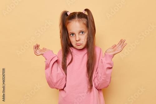 Canvastavla Puzzled uncertain little girl with ponytails wearing pink sweatshirt posing isolated over beige background shrugging shoulders looking with pout lips doesn't know answer