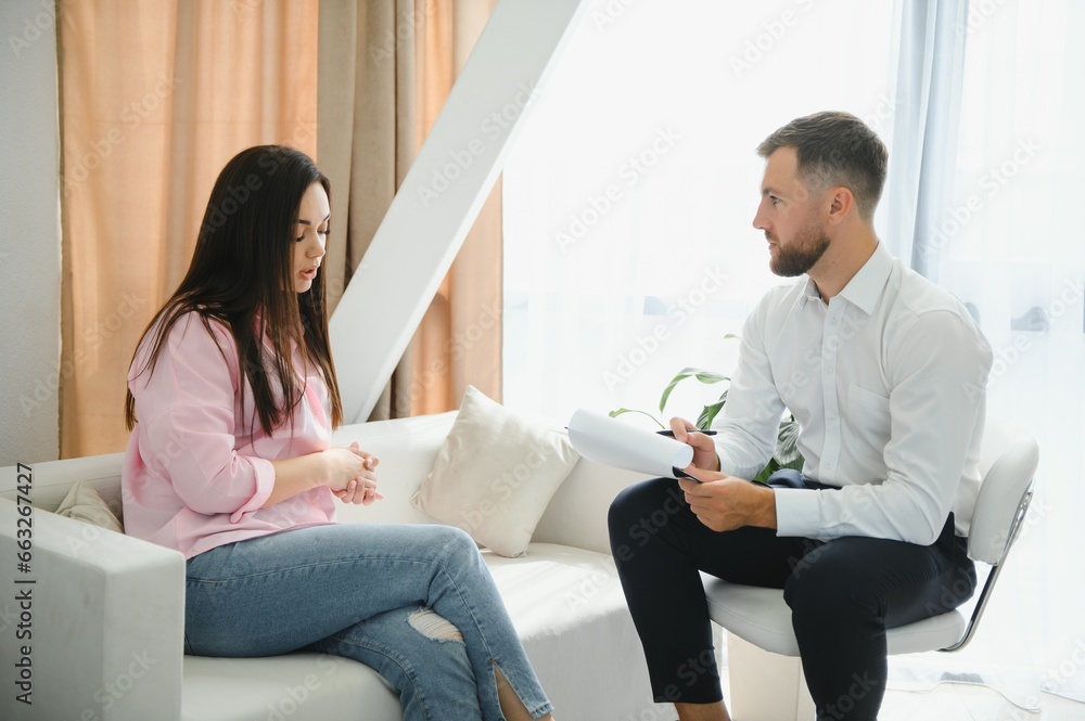Psychologist taking notes during therapy session with sad young woman in his office. Copy space Psychologist taking notes during therapy session with sad young woman in his office. Copy space