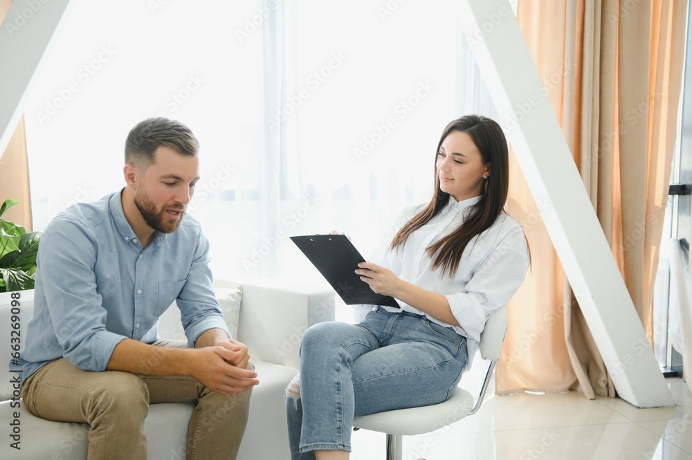 Psychologist talking with patient on therapy session. Depressed man speaking to a therapist while she is taking notes Psychologist talking with patient on therapy session. Depressed man speaking to a therapist while she is taking notes