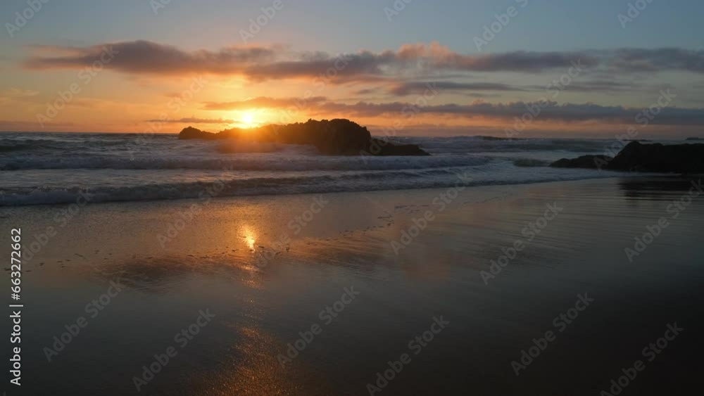 Sandy Ocean shore with rolling waves with an orange sun on the horizon at sunset. Sand beach with rolling waves hitting a big rock. Contemplation of the sea waves during sunset. Slow motion. . Sandy Ocean shore with rolling waves with an orange sun on the horizon at sunset. Sand beach with rolling waves hitting a big rock. Contemplation of the sea waves during sunset. Slow motion. .