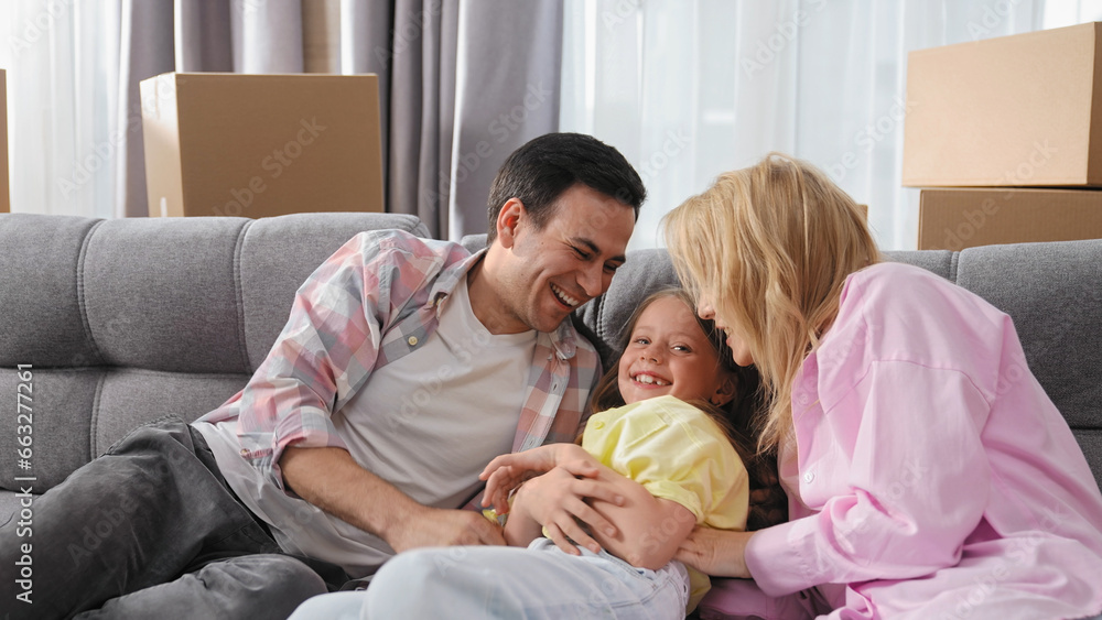 Joy parents play game with cute little kid. Happy family hug cozy sofa. Funny girl laugh. Smile child have fun. People tickling baby. Mom move into new home. Parenthood laughter. Dad buy real estate.