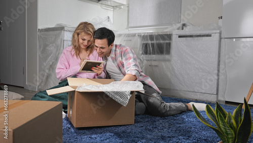 Couple move into new house. People pull things out box. Family unpack stuff. Home relocation. Real estate concept. Girl sit floor package item. Adult man buy flat. Team work unbox. Bubble wrap goods. photo