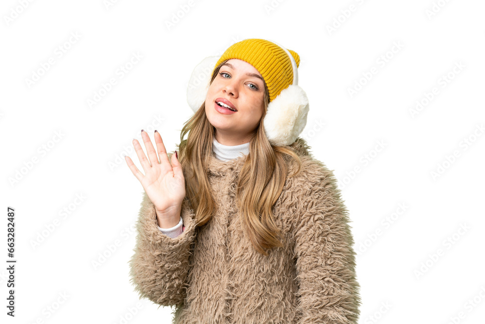 Young girl wearing winter muffs over isolated chroma key background saluting with hand with happy expression Young girl wearing winter muffs over isolated chroma key background saluting with hand with happy expression