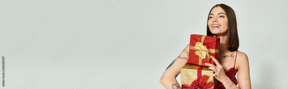 happy woman with red presents in hands looking away on ecru backdrop, holiday gifts concept, banner happy woman with red presents in hands looking away on ecru backdrop, holiday gifts concept, banner