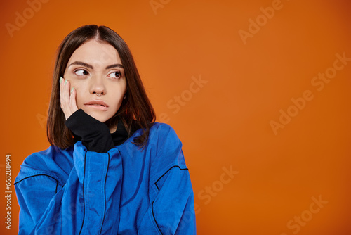 pensive woman with pierced nose biting lip and looking away on orange background, hand near face © LIGHTFIELD STUDIOS
