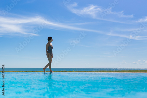 Beautiful woman in a swimming suit walking around the edge of the pool on vacation. © bignai