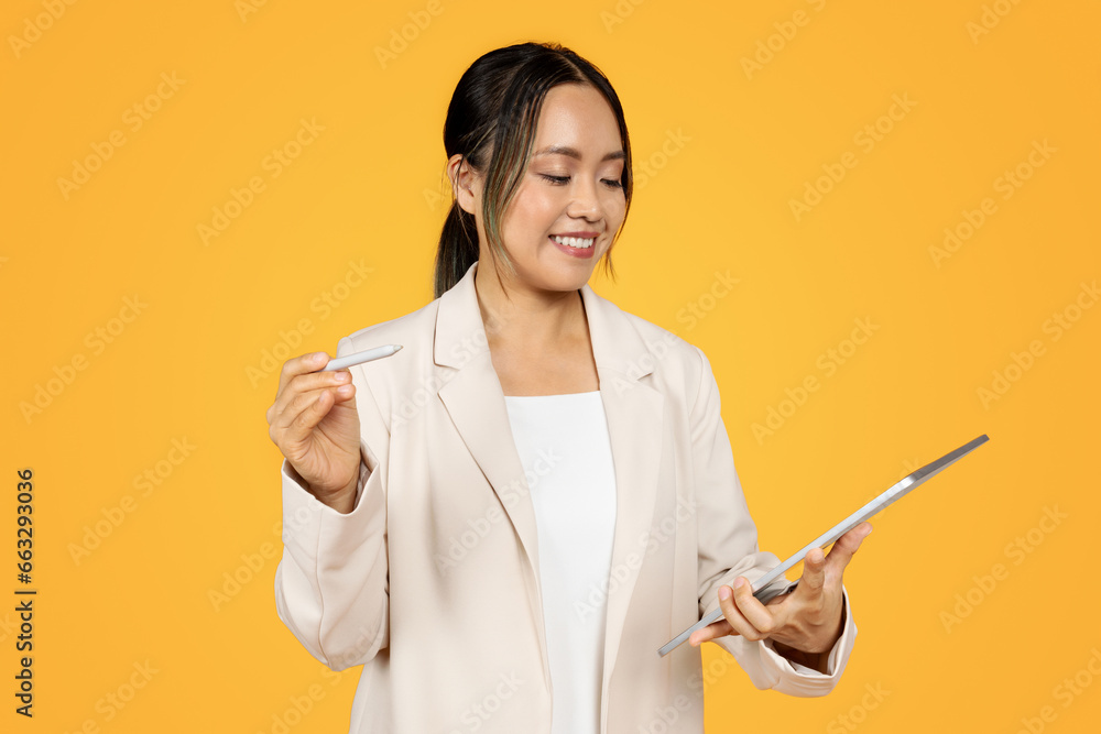 Woman holding tablet, yellow background. Woman smiling with stylus, studio Woman holding tablet, yellow background. Woman smiling with stylus, studio