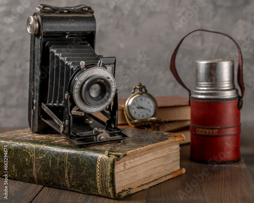 Antique bellows camera on an antique book with a thermos of coffee and a pocket watch next to it photo