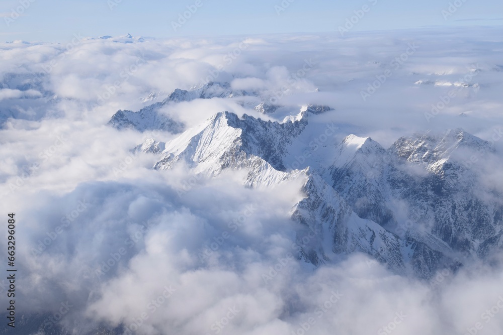 Breathtaking aerial view of alpine snowcapped mountain range peaking through heavy clouds. Mountain peaks of the Ötztal Alps from above. The impressive winter view is taken from an airplane window.