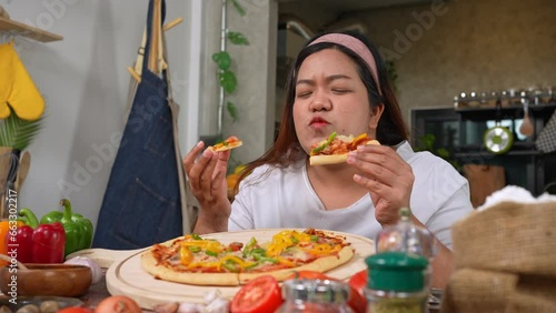 Happy Asian woman eating homemade pizza in home after baked pizza. Overweight women enjoy eating. Concept of binge eating disorder BED and Relaxing with Eating junk food and unhealthy foods.
