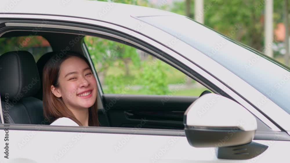 Happy Asian woman sitting in car behind steering and wave hand. Concept of happy driver, car insurance service. Customers excited after buying new car, new drivers excited for successful car license Happy Asian woman sitting in car behind steering and wave hand. Concept of happy driver, car insurance service. Customers excited after buying new car, new drivers excited for successful car license