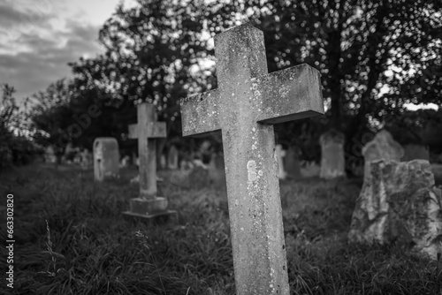 Shallow focus of a being stone crucifix seen in a seaside cemetery in the UK. The grave appears to be leaning over in the soft earth.