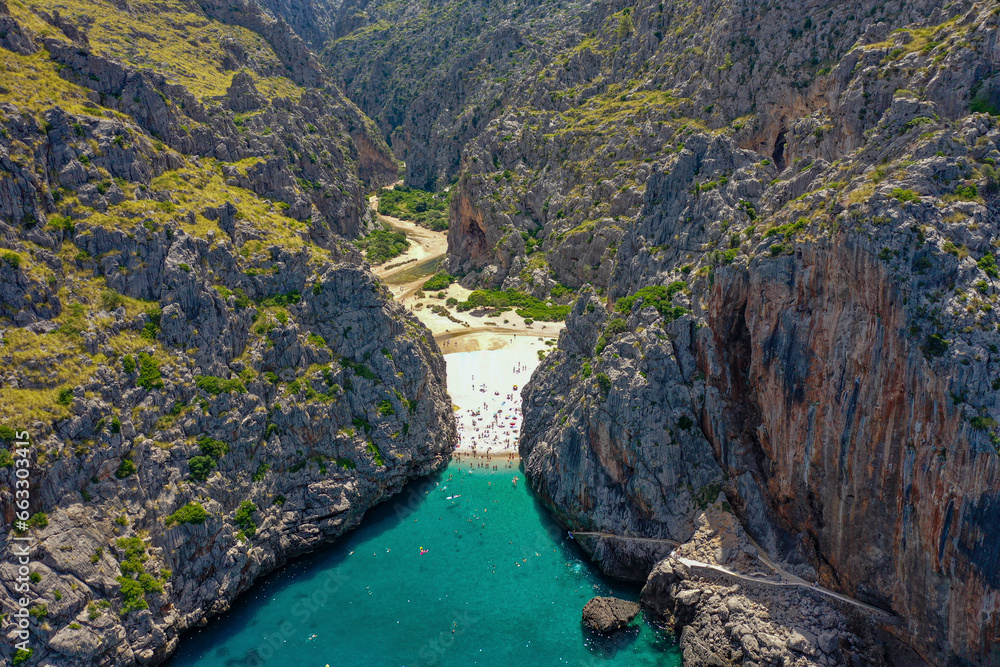 Aerial view of Sa Calobra beach with people swimming in the clear blue water between the narrow rocky valley of Torrent de Pareis in Balearic Islands, Spain. Aerial view of Sa Calobra beach with people swimming in the clear blue water between the narrow rocky valley of Torrent de Pareis in Balearic Islands, Spain.