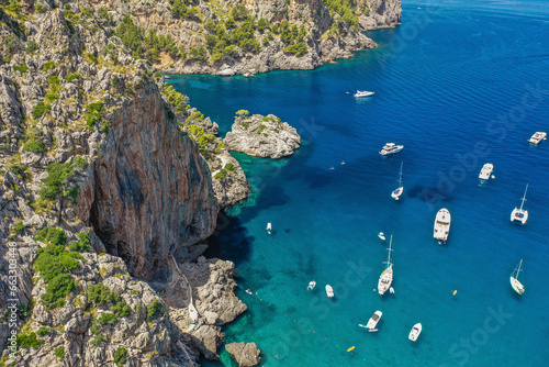 Aerial view of boats, yachts and sailboats in clear blue waters next to a rocky mountain by Sa Calobra beach in Balearic Islands, Spain. photo
