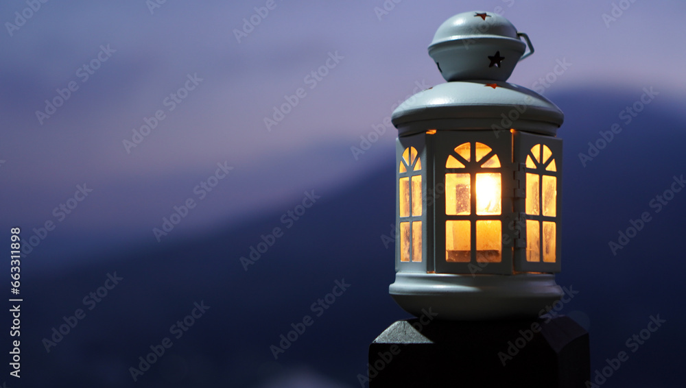 Old lantern light with candle inside at night. Lights of the lantern shine in the evening on soft dark blue background. Copy space. Inspirational backgrounds.