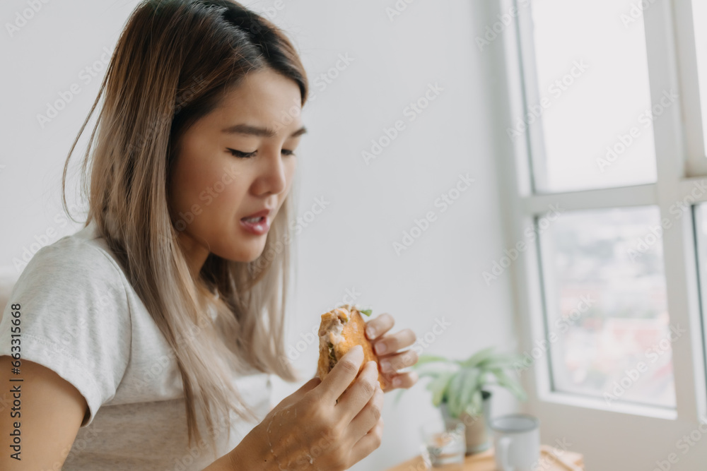 Asian Thai woman having homemade breakfast, eating sandwich hungrily at home alone. Asian Thai woman having homemade breakfast, eating sandwich hungrily at home alone.